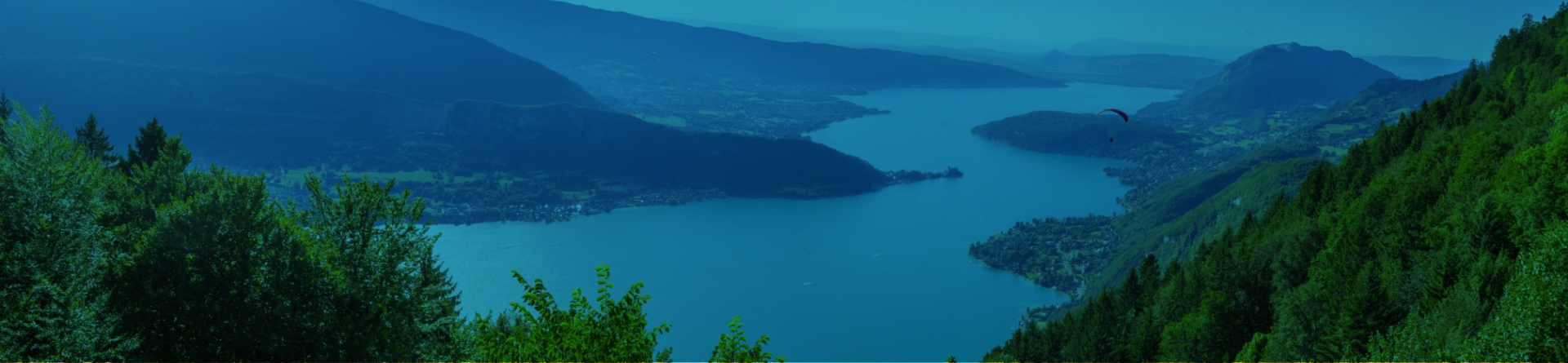 Vue panoramique du lac d&rsquo;Annecy entour&eacute; de montagnes avec parapente en vol